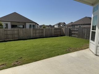 A spacious backyard with a lush green lawn and fenced privacy in Blackhawk by Chesmar Homes (Pflugerville, TX).