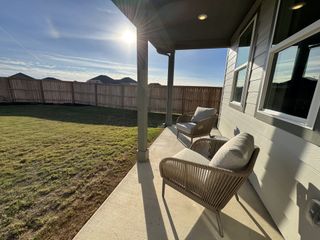 Model Home A cozy patio with cushioned chairs overlooks a sunlit, fenced backyard, creating a serene outdoor retreat.