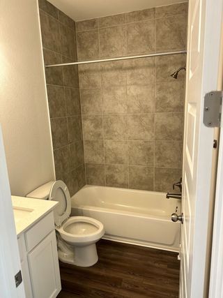 Model Home A modern bathroom featuring a tiled shower, white vanity, and sleek wood flooring.