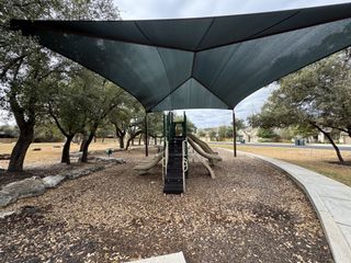 A well-equipped playground with slides and climbing structures sits under a large shade canopy in Lakeside at Lake Georgetown by Coventry Homes (Georgetown, TX).