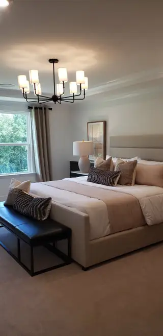 Model Home A cozy bedroom featuring a plush bed, elegant chandelier, and natural light from a large window with serene views.