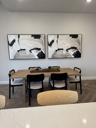 A modern dining area featuring a wooden table, black chairs, and abstract artwork, creating a stylish and inviting space.