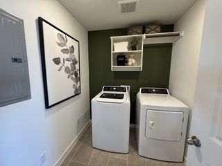 A chic laundry room with modern washer and dryer, olive green accent wall, and stylish shelving.