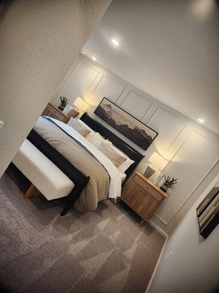 A cozy bedroom with warm lighting, taupe bedding, wooden furniture, and modern artwork creates a serene retreat.