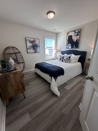 A cozy bedroom featuring modern art, sleek wood floors, and a plush bed with textured bedding and a stylish accent chair.