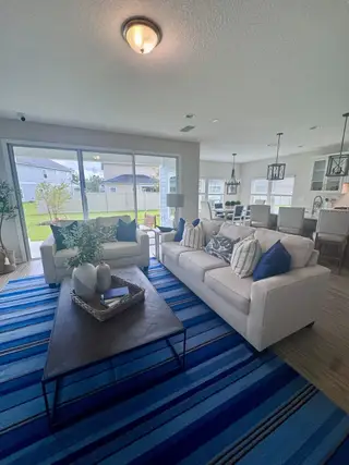 Model Home A cozy living area with white sofas, blue accents, and an open layout leading to a spacious kitchen and dining space.