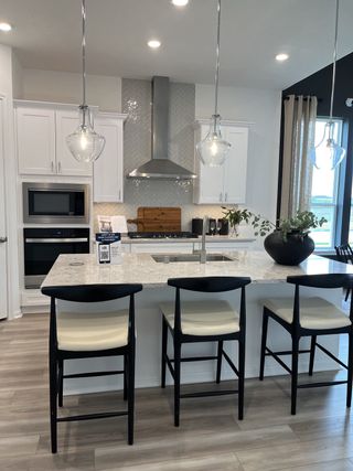 A modern kitchen with sleek white cabinets, an island with black chairs, and stylish pendant lighting.