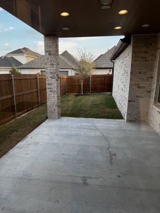 A cozy backyard patio with brick columns, recessed lighting, and a fenced lawn for outdoor enjoyment.