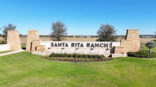 Street view Elegant stone entrance at Santa Rita Ranch by Westin Homes, showcasing lush landscaping in Liberty Hill, TX.