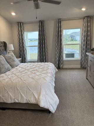 A cozy bedroom with a tufted headboard, plush bedding, patterned drapes, and large windows overlooking a serene view.