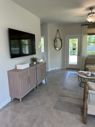 A cozy living space with sleek tile flooring, a wall-mounted TV, and a chic cabinet, accented by natural light.