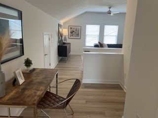 A contemporary living area with a cozy seating area, stylish desk, and ample natural light through large windows.