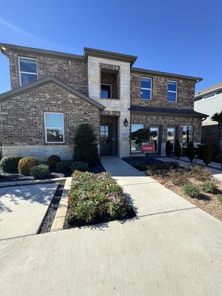 A brick and stone home with a "LAVACA" sign, featuring a paved walkway, landscaping, and a sunny sky in Lisso by Taylor Morrison, Pflugerville, TX.
