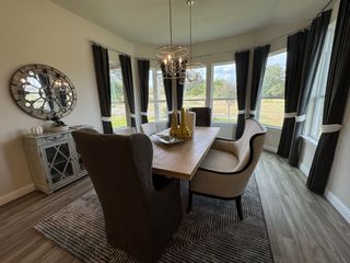 A cozy dining room with a wooden table, modern chandelier, and large windows overlooking a serene landscape.