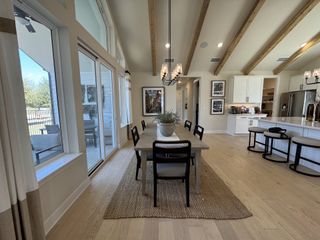 An open-concept dining area with vaulted ceilings, wooden beams, and large windows, adjacent to a modern kitchen.