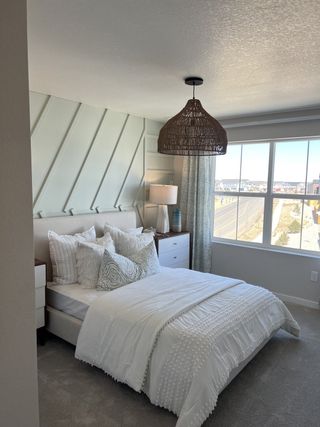 A cozy bedroom with soft textures, stylish bedding, and a woven pendant light, bathed in natural light from a large window.