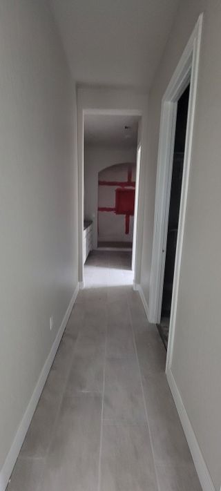 A long, neutral-toned hallway leading to different rooms, with construction elements such as unfinished trim work and door installations still in progress.