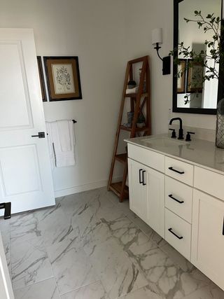 A chic bathroom with marble floors, sleek white vanity, black fixtures, and stylish shelving.