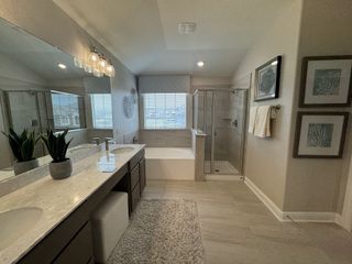 Model Home A modern bathroom with a double vanity featuring a gray granite countertop, a glass-enclosed shower, a soaking tub, and neutral-toned tile flooring.