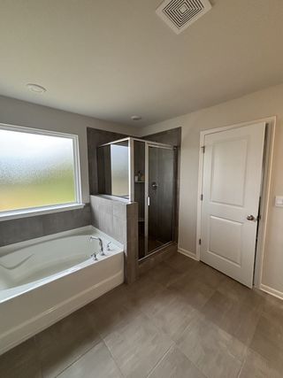 A modern bathroom with a spacious bathtub, glass-enclosed shower, and light tile flooring.