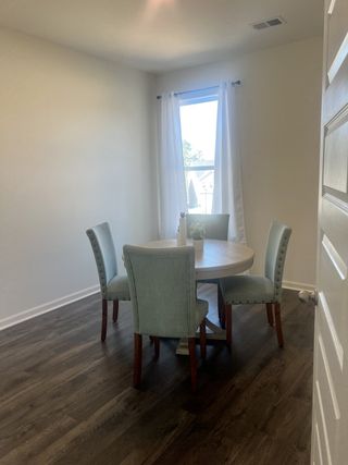 A quaint dining area featuring a round table with upholstered chairs, white curtains, and hardwood flooring.