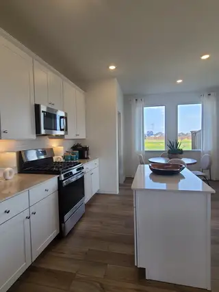 Model Home A modern kitchen featuring white cabinets, a sleek island, and a cozy dining area with large windows.