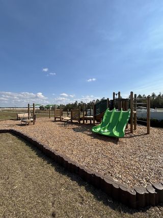 A scenic playground with wooden structures, bright green slides, and plenty of space for outdoor fun in Gardenia Reserve by Mattamy Homes (Apopka, FL).