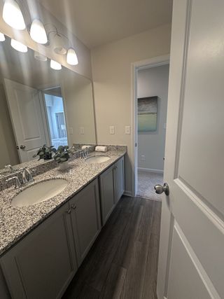 Model Home A chic bathroom featuring dual sinks with granite countertops and elegant lighting, complemented by wood-look flooring.