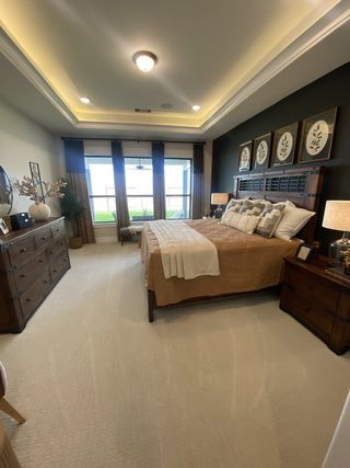 A cozy bedroom featuring tray ceilings, elegant lighting, dark accent wall, and large windows with natural light.