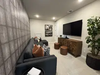 A cozy media room with a dark sectional sofa, decorative wall art, round stools, and a large TV for entertainment.