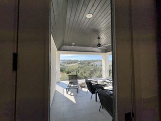 A glimpse through an open doorway onto a covered patio with outdoor furniture and a scenic view of the surrounding landscape.