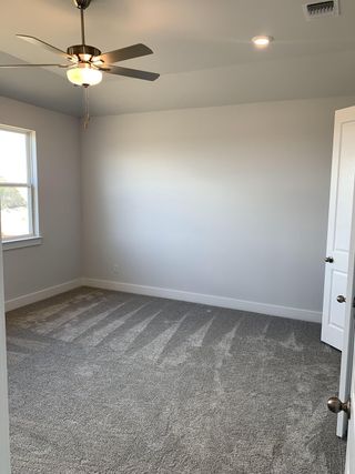 Model Home A cozy bedroom with plush carpet, neutral walls, and a ceiling fan offers a serene retreat.