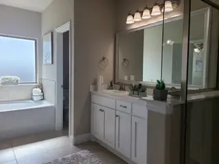 Model Home A bright bathroom with a spacious vanity, framed mirror, large tub, and sleek lighting for a modern touch.