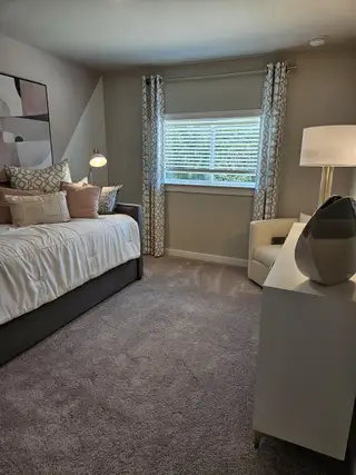 Model Home A cozy bedroom with soft carpeting, a plush bed, elegant curtains, modern artwork, and warm lighting completes the serene atmosphere.