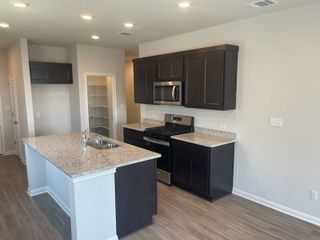 A modern kitchen with dark cabinets, granite countertops, an island sink, and stainless steel appliances.