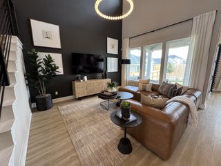 A stylish living room featuring a leather sectional, dark accent wall, modern decor, and large windows with ample natural light.
