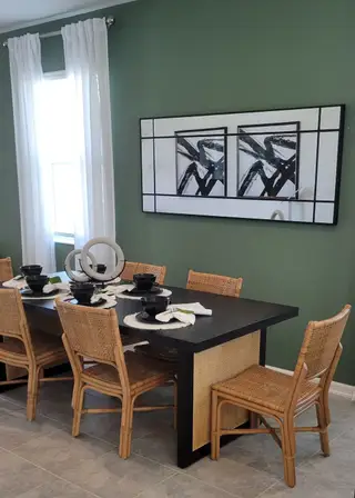 Model Home A chic dining area with a dark table, wicker chairs, green walls, and abstract art for a modern touch.