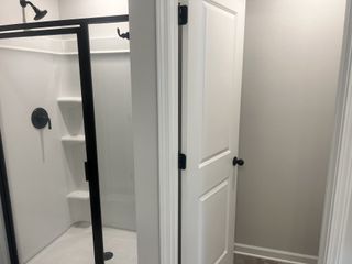 Model Home A modern bathroom showcases a sleek black-framed shower with a white interior, adjacent to a classic white door with matte black hardware.