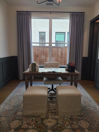 A cozy home office featuring a stylish desk, elegant drapes, and a patterned area rug for a refined workspace.