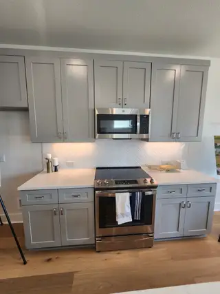 A modern kitchen with sleek gray cabinets, stainless steel appliances, and a herringbone tile backsplash.
