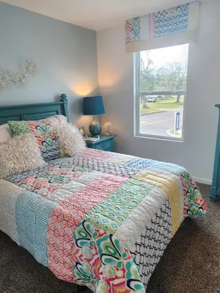 A cozy bedroom with colorful patterned bedding, plush pillows, and a chic blue lamp creating a vibrant and inviting space.