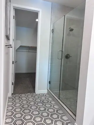 Model Home A bathroom with hexagonal tile flooring, a sleek glass shower, and a walk-in closet entry.