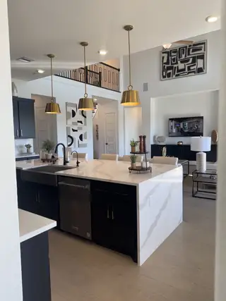 Model Home A modern kitchen with a spacious marble island, black cabinetry, and elegant gold pendant lighting.