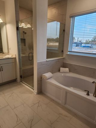 A luxurious bathroom featuring a marble-tiled shower, elegant bathtub, and ample natural light through a large window.
