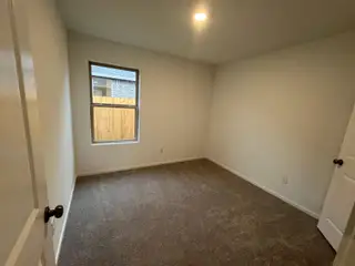Model Home A cozy bedroom with neutral walls, plush carpet, and a single window allowing natural light to brighten the space.