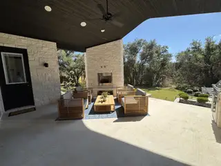 A modern patio with sleek wooden seating, stone fireplace, and open views of lush greenery.