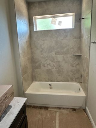 Model Home A modern bathroom under construction featuring a bathtub with elegant tiled walls and a sleek window for natural light.