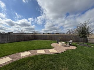 Model Home A beautifully landscaped backyard with a stone fire pit and lush greenery in August Fields by Chesmar Homes (New Braunfels, TX).