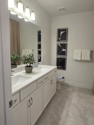 A sleek bathroom with dual sinks, elegant lighting, modern art, and a touch of greenery.