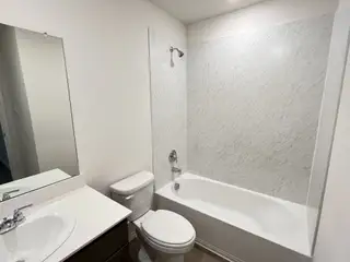 A modern bathroom with a bathtub-shower combination, white vanity, and bright lighting.